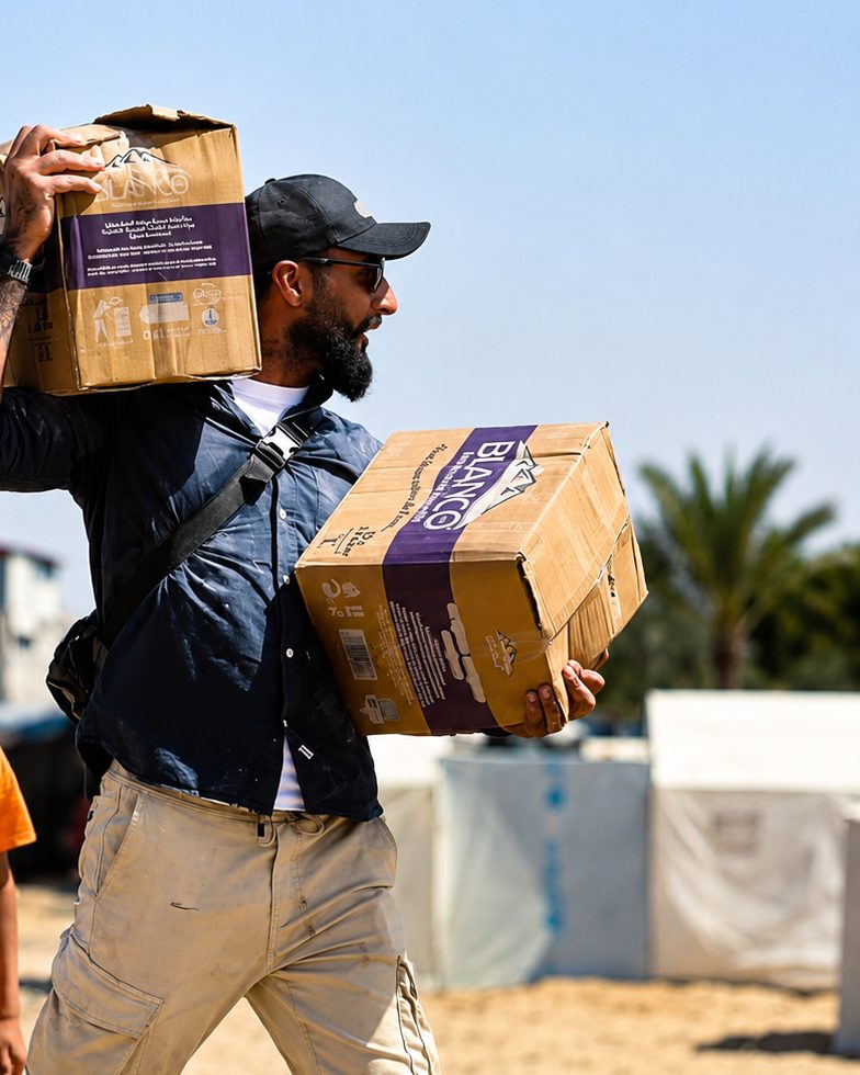 Benjamin Grant carrying cases of water through a displacement camp in Gaza