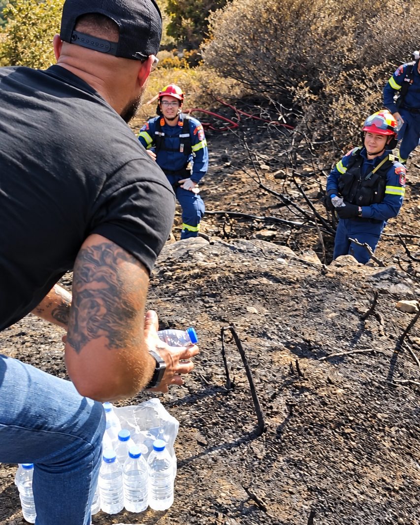 Benjamin Grant handing water to firefighters on a burnt hillside in Greece